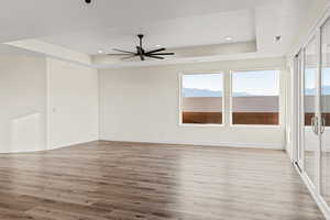 Spare room featuring a raised ceiling, wood finished floors, a ceiling fan, recessed lighting, and baseboards