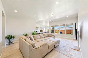 Living room with light wood-style floors, baseboards, lofted ceiling, recessed lighting, and a textured ceiling