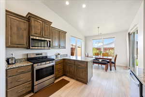 Kitchen featuring appliances with stainless steel finishes, light stone countertops, light wood-type flooring, a peninsula, and pendant lighting
