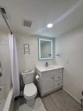 Full bathroom featuring vanity, toilet, wood finished floors, and shower / bath combination with curtain