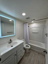 Bathroom with vanity, shower / tub combo with curtain, toilet, wood finished floors, and recessed lighting