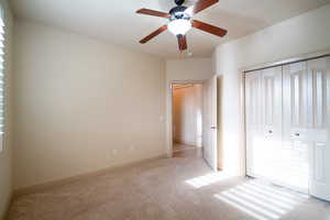Unfurnished bedroom featuring light colored carpet, a closet, baseboards, and ceiling fan