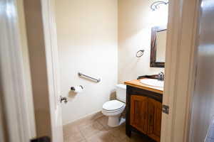 Half bathroom featuring toilet, vanity, tile patterned floors, and baseboards