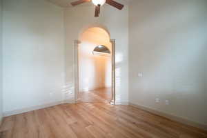 Empty room with arched walkways, ceiling fan, light wood finished floors, and baseboards