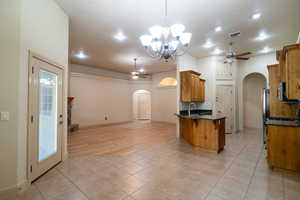 Kitchen featuring arched walkways, a ceiling fan, brown cabinetry, light tile patterned floors, and recessed lighting