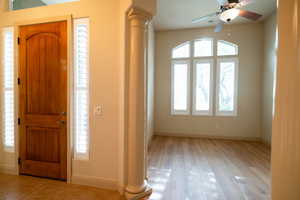 Foyer featuring ornate columns, baseboards, a ceiling fan, and light wood finished floors