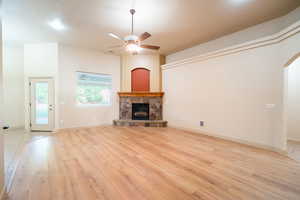 Unfurnished living room featuring ceiling fan, light wood finished floors, a fireplace, arched walkways, and baseboards