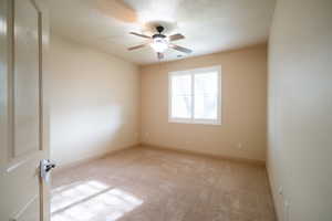 Carpeted empty room with a ceiling fan and baseboards