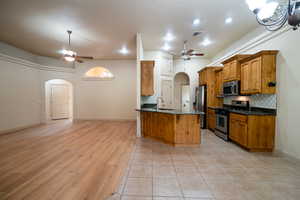Kitchen with stainless steel appliances, ceiling fan, arched walkways, brown cabinets, and recessed lighting
