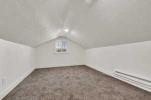 Bonus room featuring baseboard heating, a textured ceiling, vaulted ceiling, and carpet floors