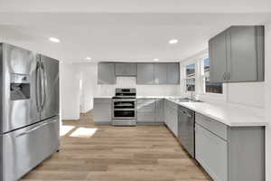 Kitchen featuring appliances with stainless steel finishes, gray cabinets, light wood-style floors, light countertops, and recessed lighting