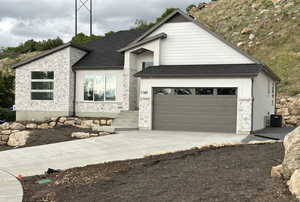 View of front of home featuring stone siding, driveway, cooling unit, and a shingled roof