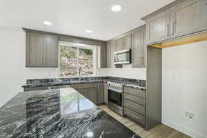 Kitchen with stainless steel appliances, a sink, dark stone counters, recessed lighting, and light wood-style flooring