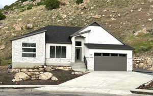View of front facade featuring stone siding, driveway, a garage, and a shingled roof