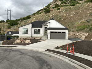 View of front facade with driveway, stone siding, roof with shingles, and a garage