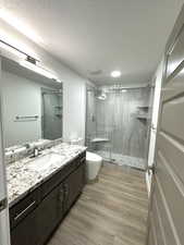 Bathroom with vanity, a stall shower, a textured ceiling, toilet, and wood finished floors
