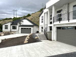 View of front of property with a garage, stone siding, a balcony, and driveway