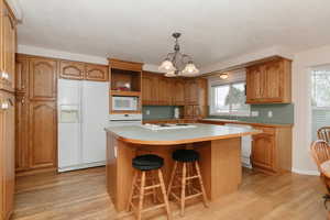 Kitchen with white appliances, light wood-style floors, brown cabinetry, and a textured ceiling