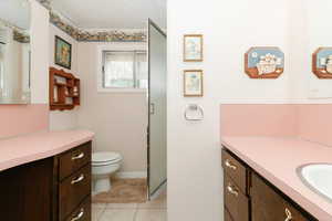 Bathroom with vanity, toilet, a stall shower, tile patterned flooring, and a textured ceiling
