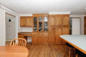 Kitchen featuring brown cabinetry, light wood-style flooring, a textured ceiling, glass insert cabinets, and light countertops