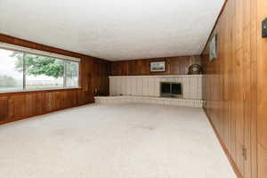 Unfurnished living room featuring wood walls, carpet, a textured ceiling, and a fireplace