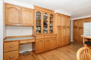 Kitchen featuring white fridge with ice dispenser, light wood finished floors, light countertops, glass insert cabinets, and brown cabinets