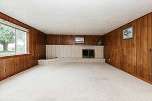 Unfurnished living room with wood walls, a fireplace, carpet floors, baseboards, and a textured ceiling