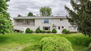 Back of house featuring a yard, a chimney, brick siding, and a balcony