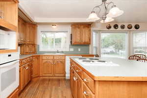 Kitchen with white appliances, light wood finished floors, a chandelier, light countertops, and brown cabinetry