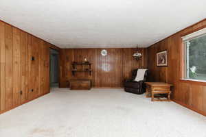 Sitting room with wood walls, a textured ceiling, carpet flooring, and baseboards