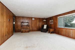 Unfurnished room with a textured ceiling, wooden walls, carpet flooring, and baseboards