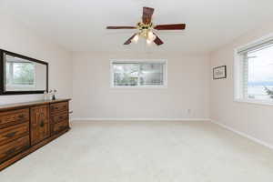 Unfurnished bedroom with light carpet, multiple windows, baseboards, and ceiling fan
