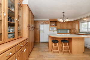 Kitchen featuring white appliances, brown cabinets, a chandelier, light wood finished floors, and glass insert cabinets