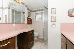 Full bathroom with vanity, a shower stall, toilet, a textured ceiling, and tile patterned flooring