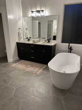 Full bath featuring a freestanding bath, double vanity, tile patterned floors, and baseboards