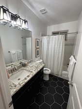 Bathroom featuring vanity, toilet, shower / bath combo with shower curtain, tile patterned floors, and a textured ceiling