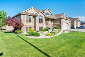 View of front of property featuring stone siding, stucco siding, concrete driveway, and a front yard