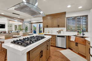 Kitchen featuring dishwasher, range hood, gas cooktop, a sink, and light countertops