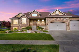 View of front facade featuring a front lawn, driveway, stone siding, a garage, and a shingled roof