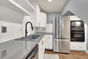 Kitchen featuring black appliances, a sink, white cabinets, decorative backsplash, and light tile patterned flooring