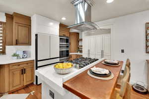 Kitchen with appliances with stainless steel finishes, island range hood, light wood-style floors, light countertops, and backsplash