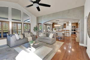Living area with high vaulted ceiling, arched walkways, a ceiling fan, healthy amount of natural light, and light wood finished floors