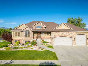 View of front of property with driveway, a front lawn, a garage, roof with shingles, and stone siding