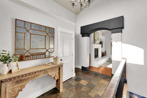 Hallway featuring stone tile flooring, a chandelier, arched walkways, and baseboards