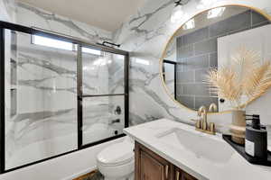 Bathroom with vanity, combined bath / shower with glass door, toilet, and tile walls