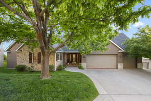 View of front of home with a garage, concrete driveway, stone siding, stucco siding, and a front lawn