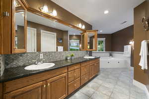 Primary bathroom with double vanity, a bath, decorative backsplash, baseboards, and recessed lighting