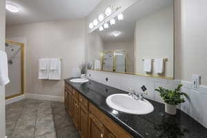 Bathroom featuring double vanity, a stall shower, and baseboards
