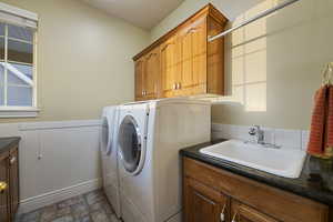 Laundry room featuring washing machine and clothes dryer, cabinet space, stone finish floors, and wainscoting