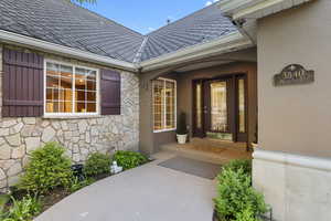 Property entrance with stone siding, stucco siding, and a shingled roof